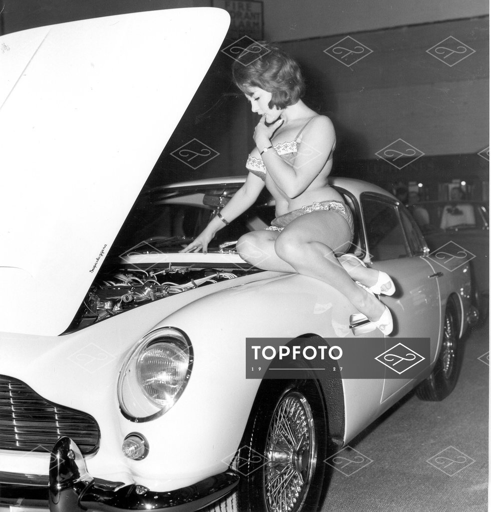 Glamorous model June Palmer sitting on a 1963 Aston Martin DB4 Vantage G.T.  at the Motor Show. Industrial exhibition - Topfoto Image Archive