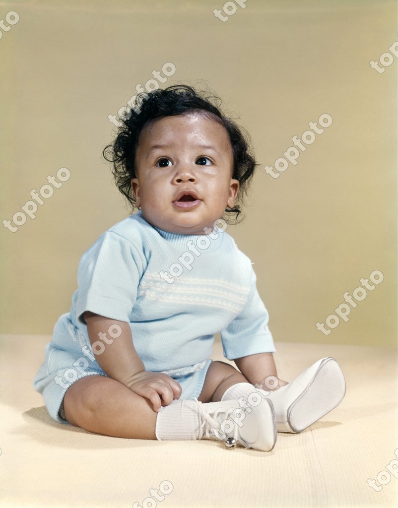 1960s PORTRAIT AFRICAN-AMERICAN BABY BOY WEARING BLUE OUTFIT WHITE SHOES  LOOKING TO SIDE - TopFoto