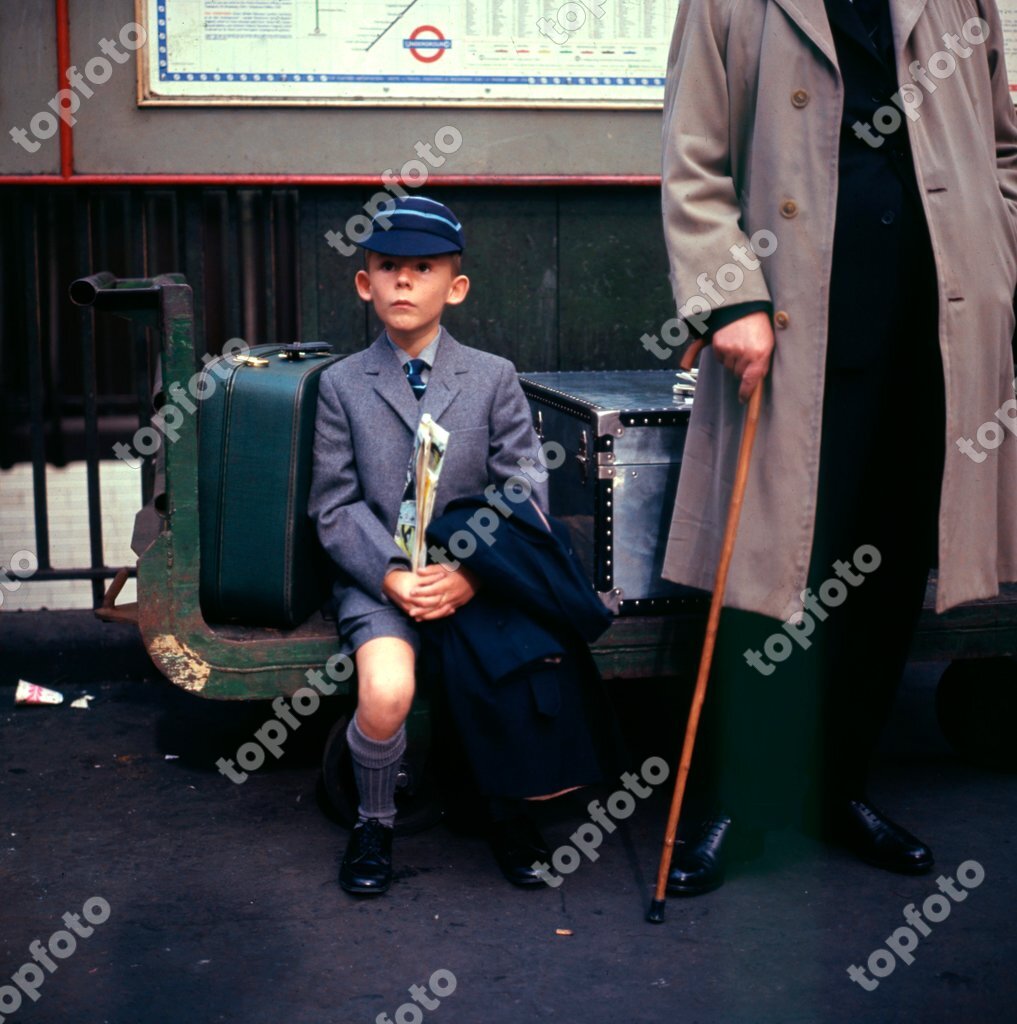 A tense , young schoolboy waits with his father on a station on his way ...